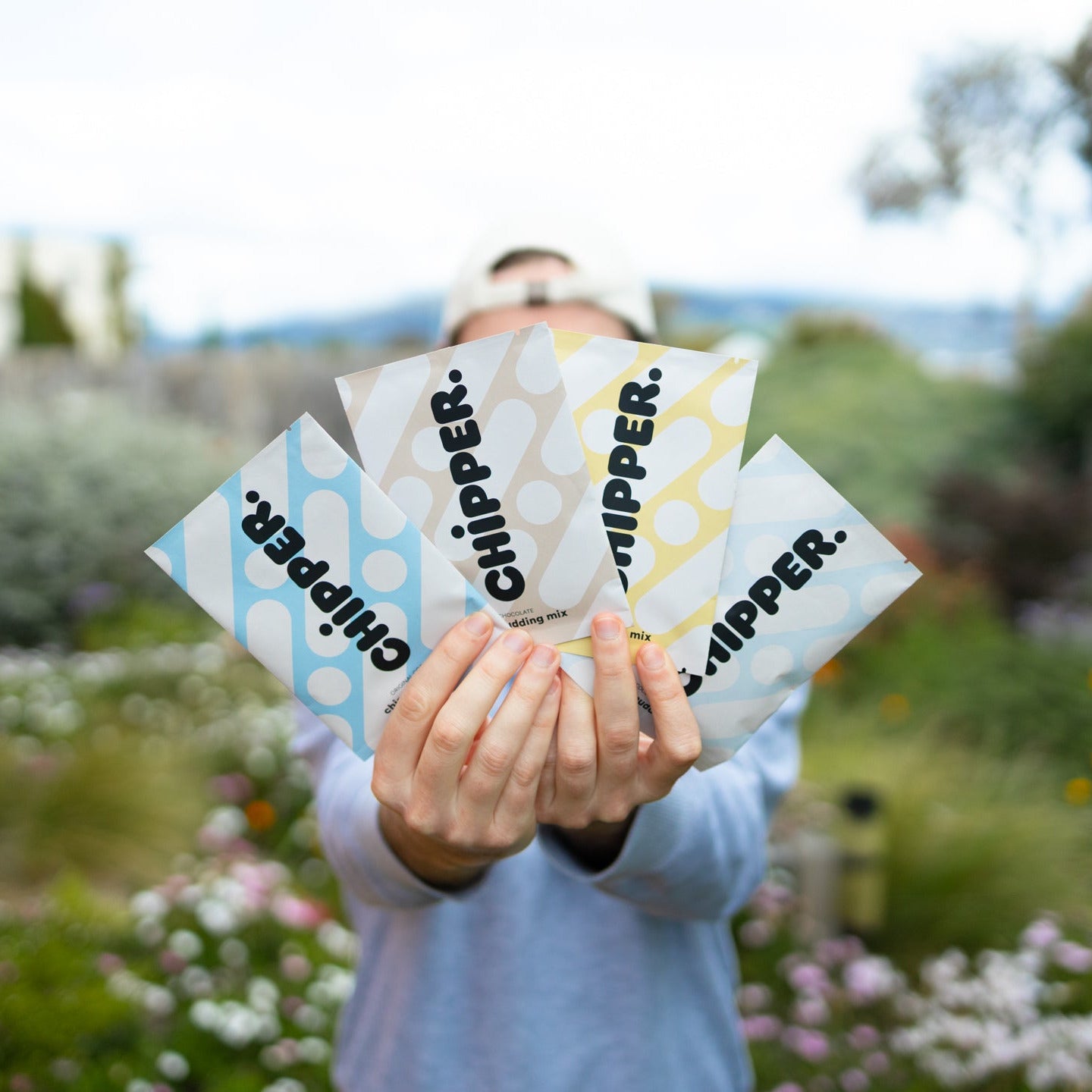 Person holding multiple 'Chipper' product packages outdoors with a garden background